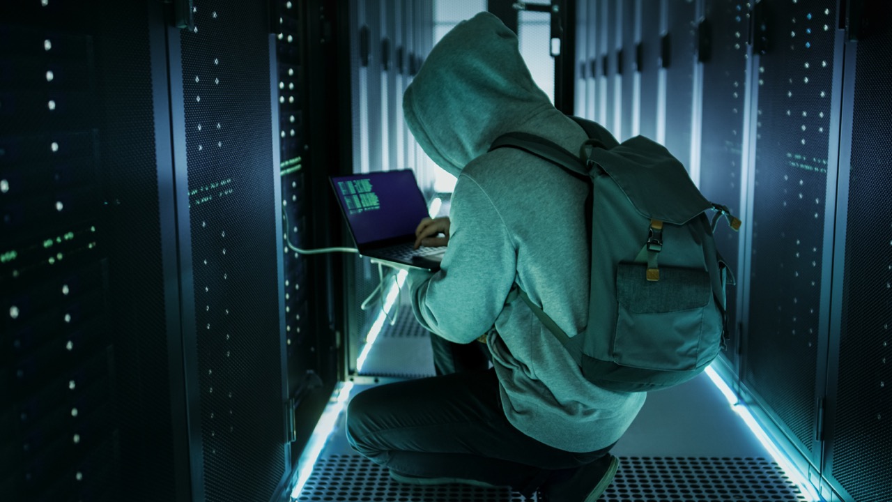 A Hooded Hacker With Laptop Connects to Rack Server and Steals Information from Corporate Data Center.